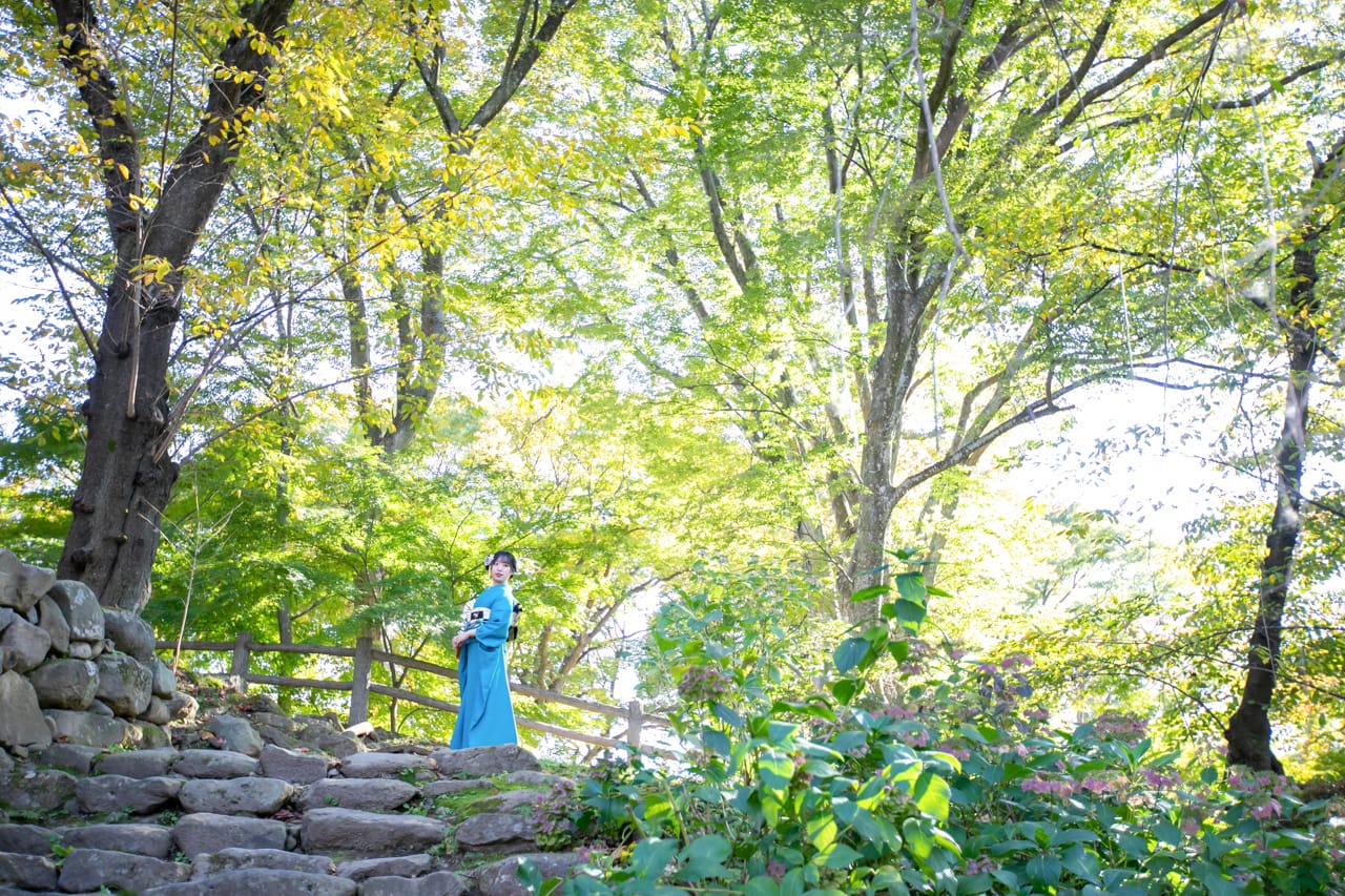 緑に囲まれた石階段の上に立つ着物の女性